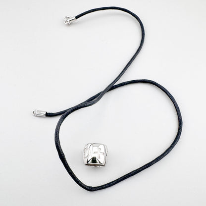 Collar con símbolos grabados sobre cordón negro, expresión sobria y contemporánea