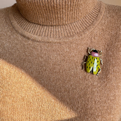 Bright green beetle brooch with golden legs worn on sweater in vintage style