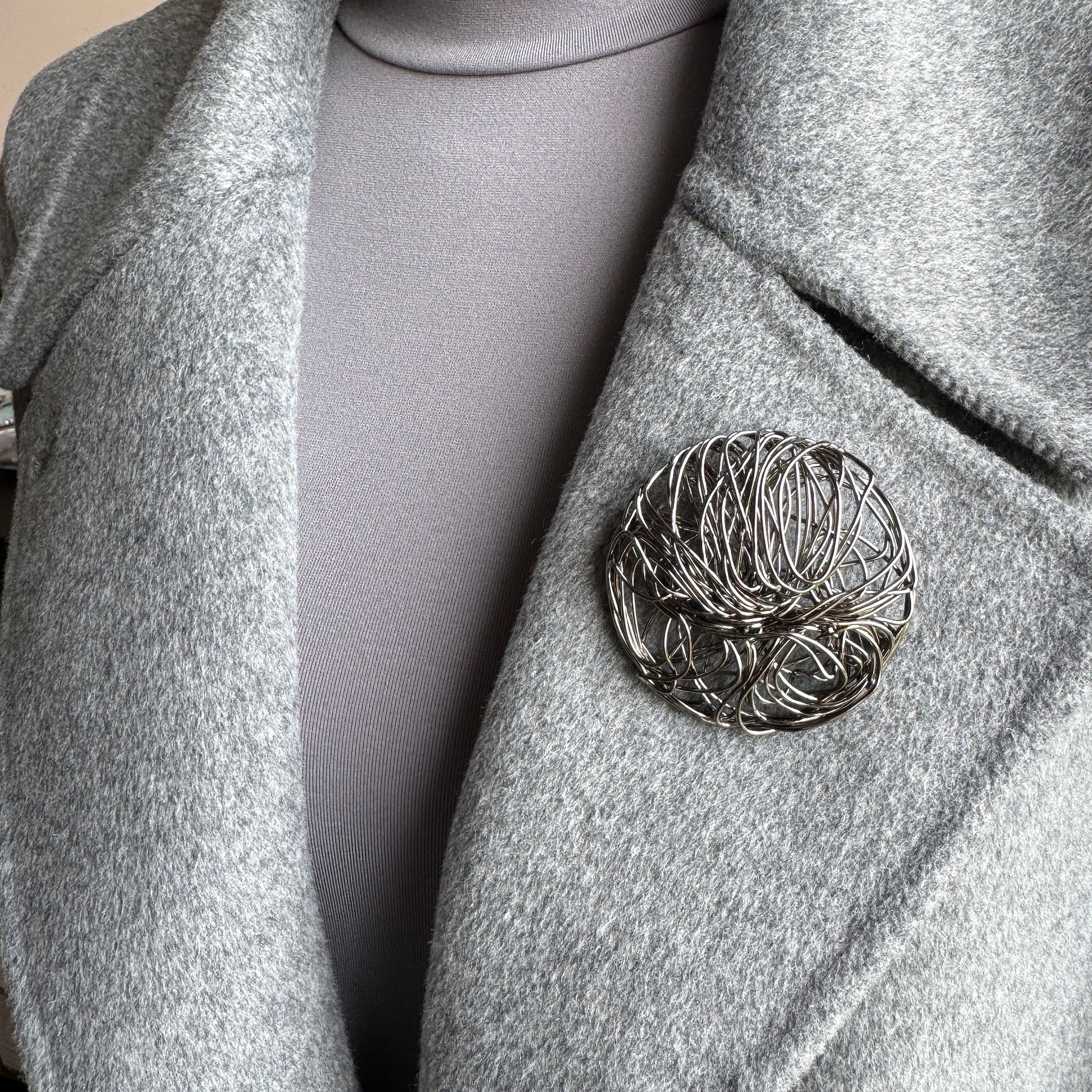 Large round geometric brooch in metal mesh design worn on coat