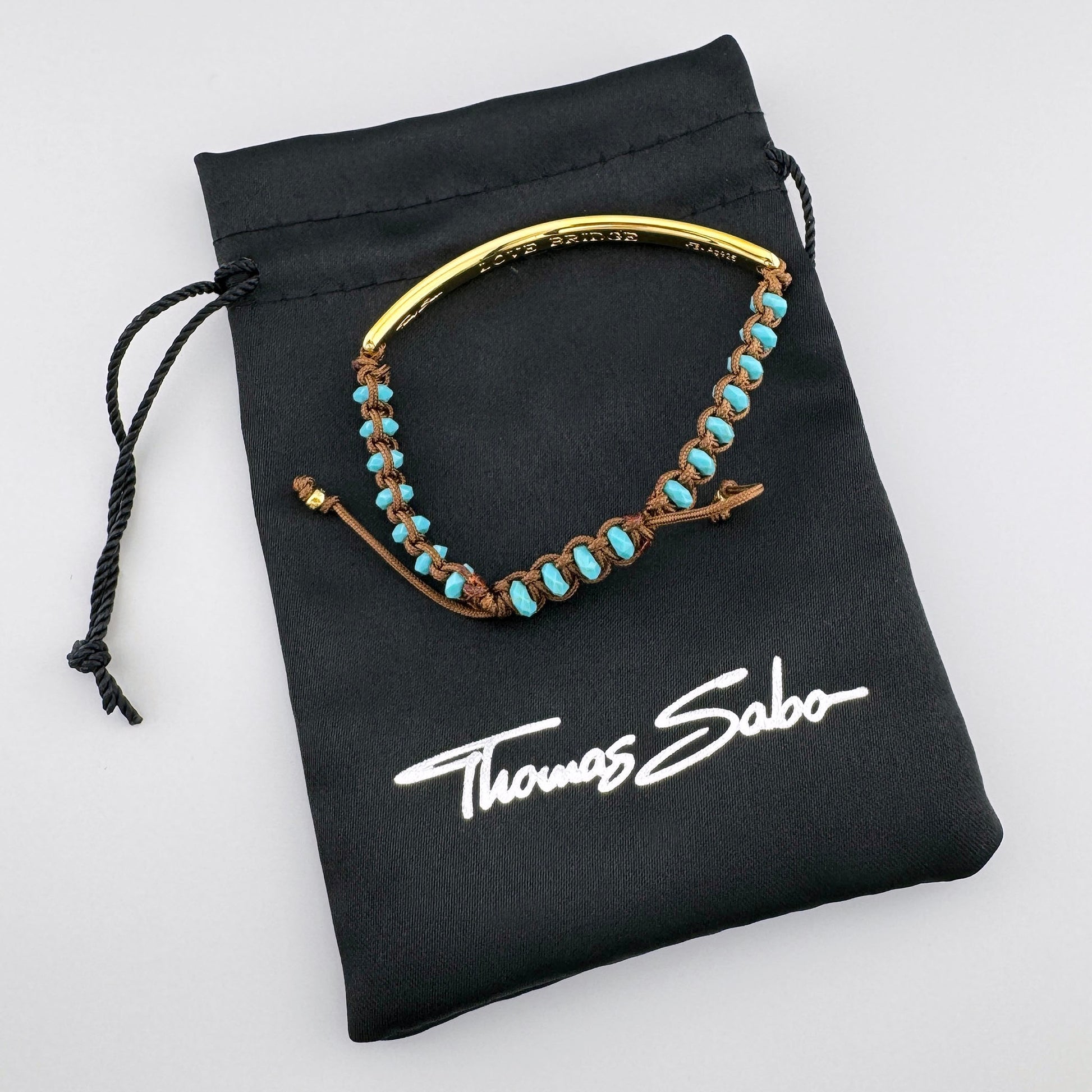 Pozłacana bransoletka Love Bridge Thomas Sabo z turkusem na czarnym firmowym woreczku