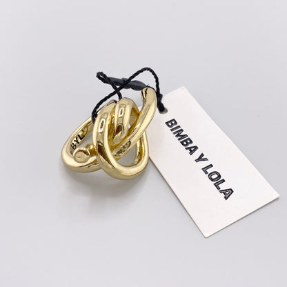 Gold-tone knot ring by Bimba y Lola shown from the side beside its branded tag