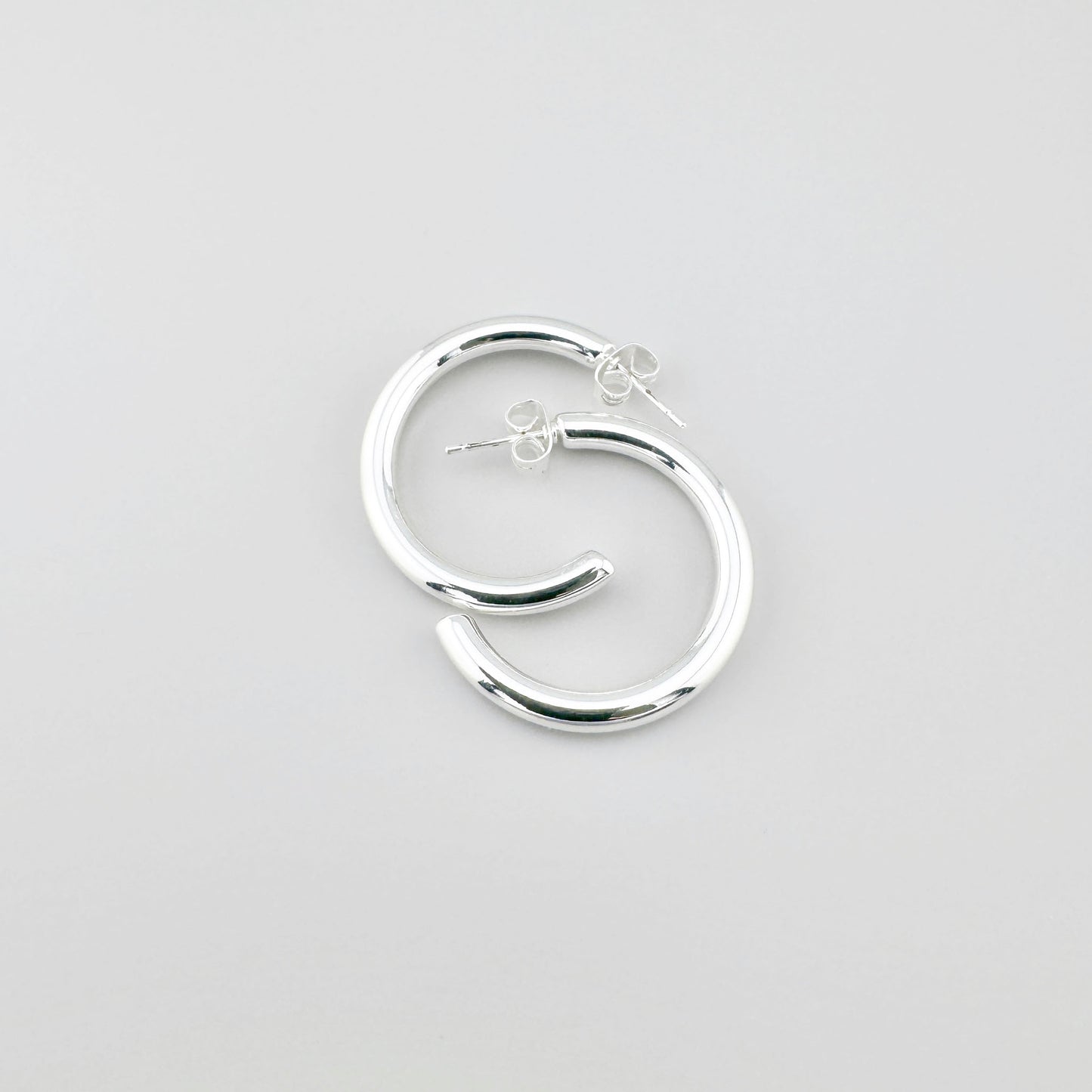 Сережки-півкільця з плакованої сталі, полірована поверхня ловить світло, чистий мінімалізм