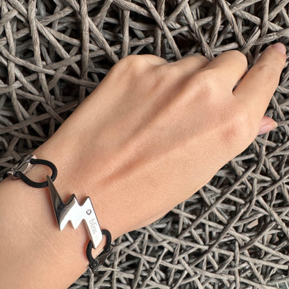 Lightning motif bracelet worn on the wrist with black rubber cords and steel detail
