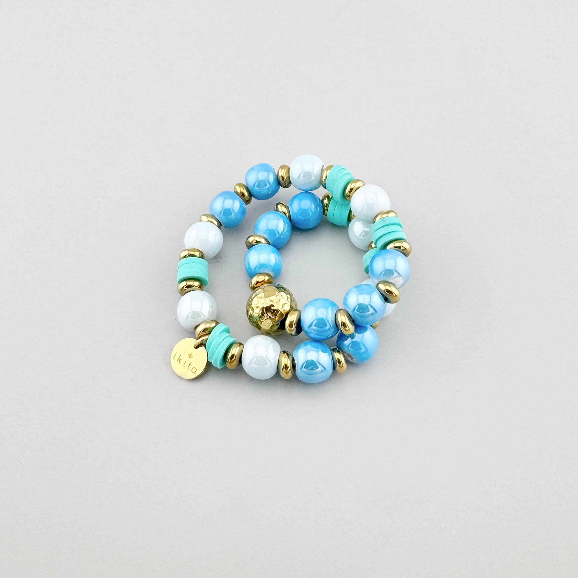 Armband aus blauen und weißen Perlen mit türkisfarbenen und goldenen Elementen, Marke Ikita.
