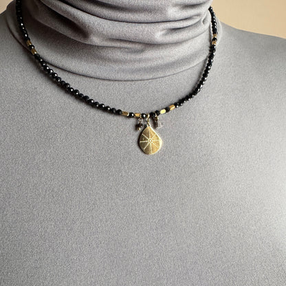 Black stone necklace IRL worn close to the neck with a gold medallion pendant