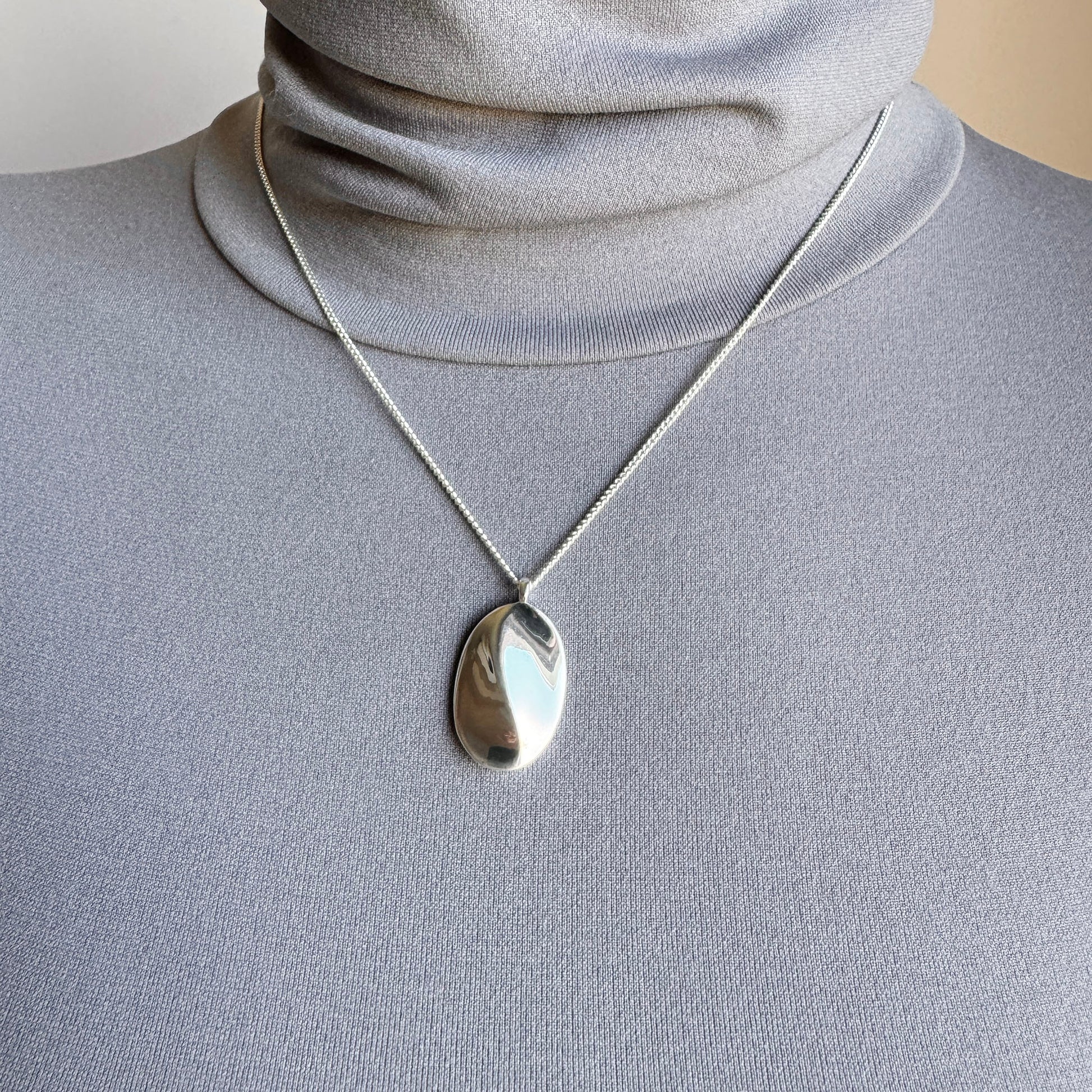 Minimalist silver necklace with an oval pendant and smooth reflective finish