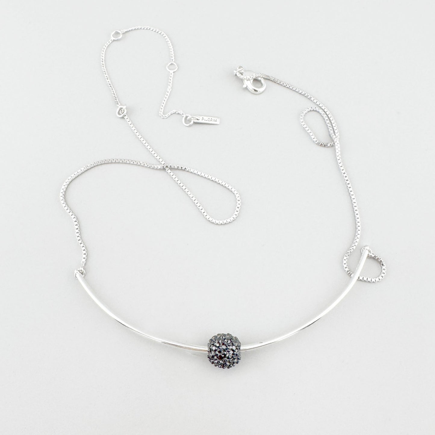 Pilgrim necklace with delicate curve and crystal sphere laid on light background
