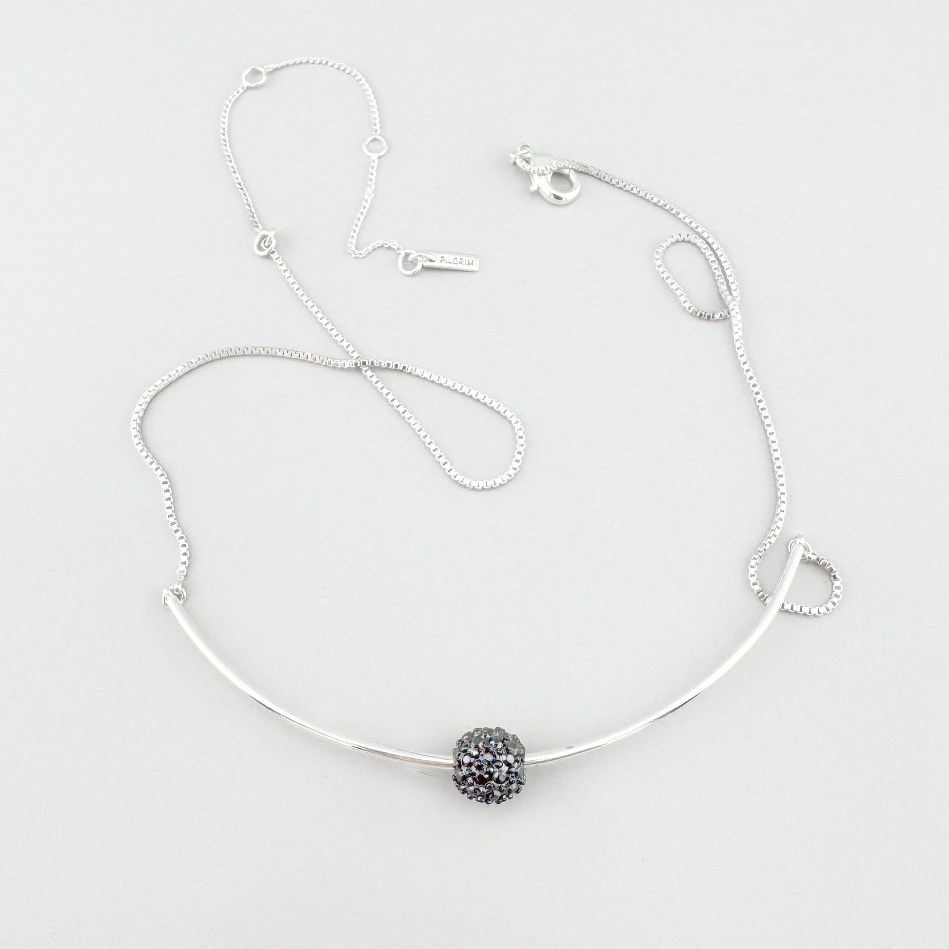 Pilgrim necklace with delicate curve and crystal sphere laid on light background
