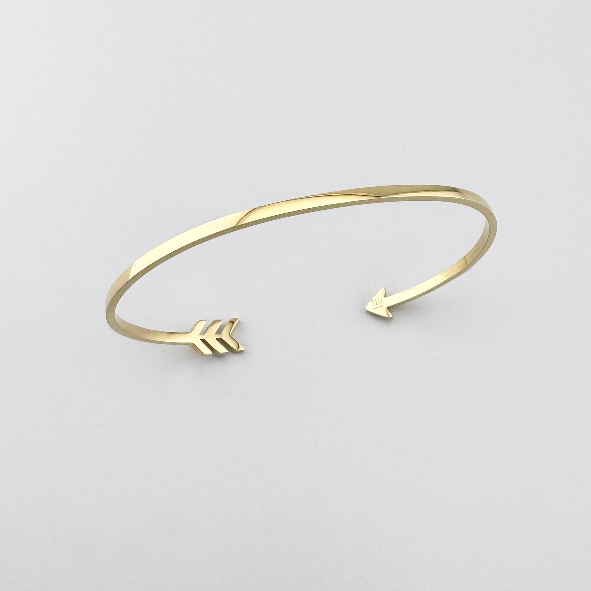 Bracelete aberto com motivo de flecha dourada criando um gesto leve e expressivo no pulso