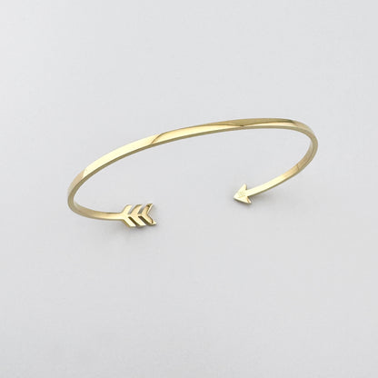 Bracelete aberto com motivo de flecha dourada criando um gesto leve e expressivo no pulso
