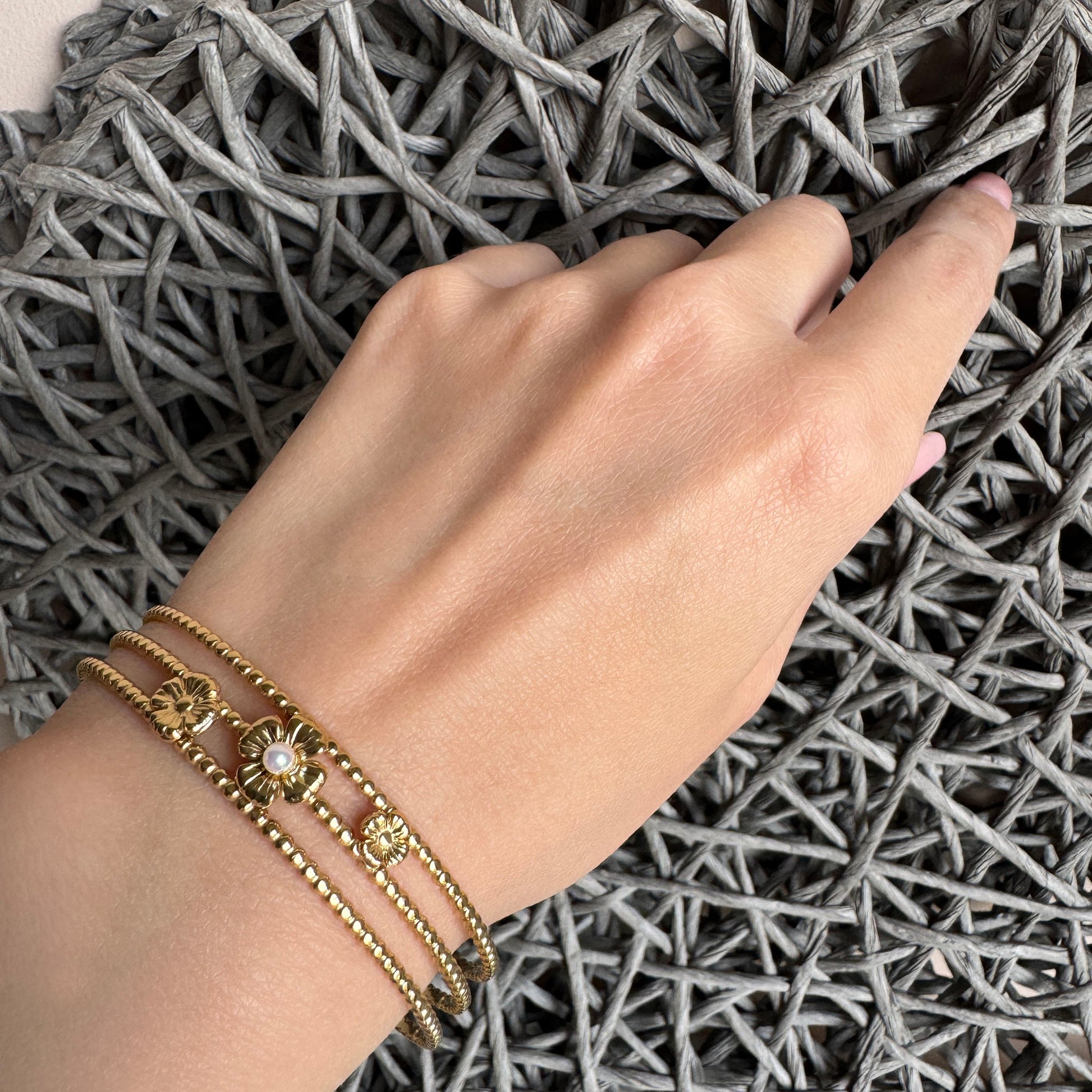Elegant gold cuff bracelet with floral and pearl details worn on wrist