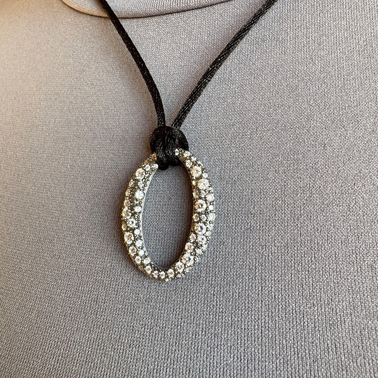 Pendentif ovale serti de zircons, halo de lumière sur cordon noir