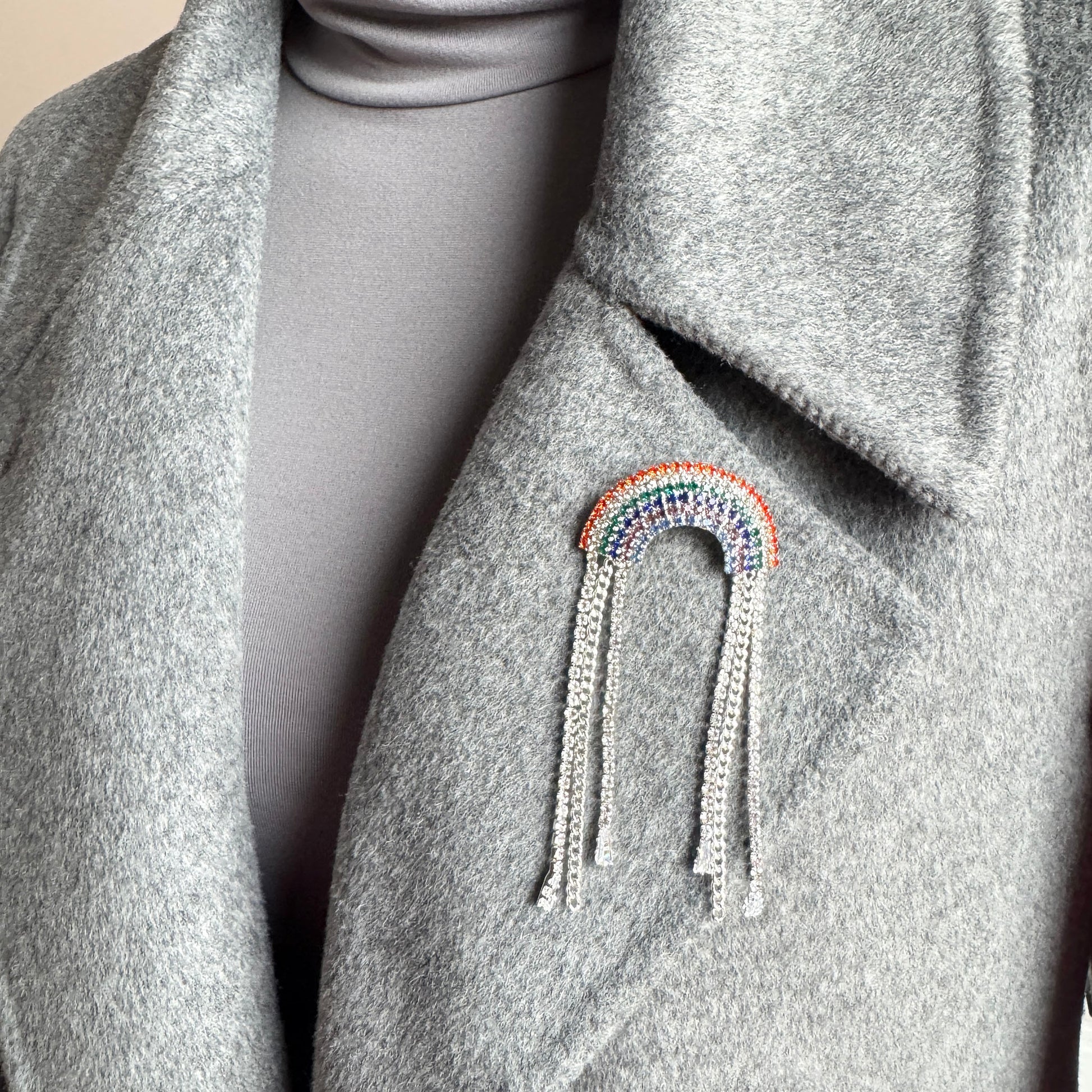 Rainbow crystal brooch Maravillas worn on a coat with multicolor sparkle and chain tassels