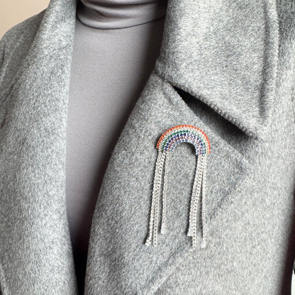Rainbow crystal brooch Maravillas worn on a coat with multicolor sparkle and chain tassels