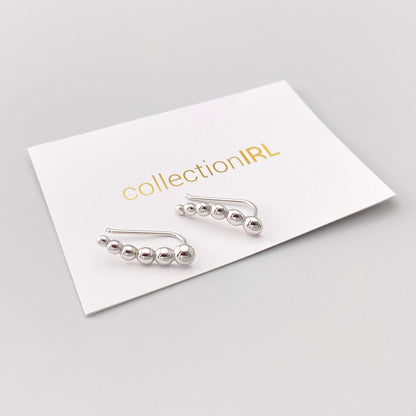 Kolczyki nausznice z gładkimi srebrnymi kuleczkami ułożone na karcie marki