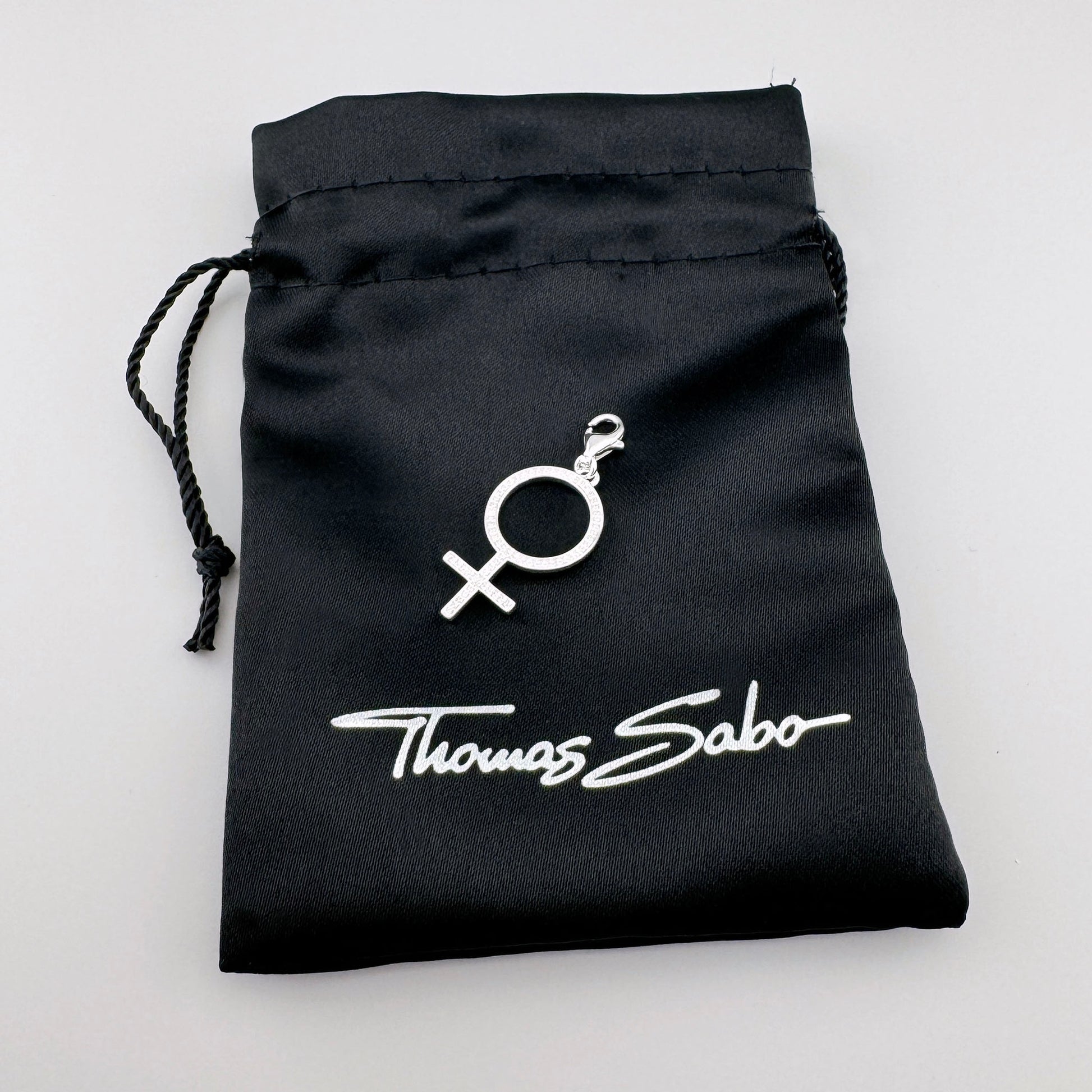 Silberner Thomas Sabo Charm mit Frauensymbol auf dem schwarzen Markenbeutel