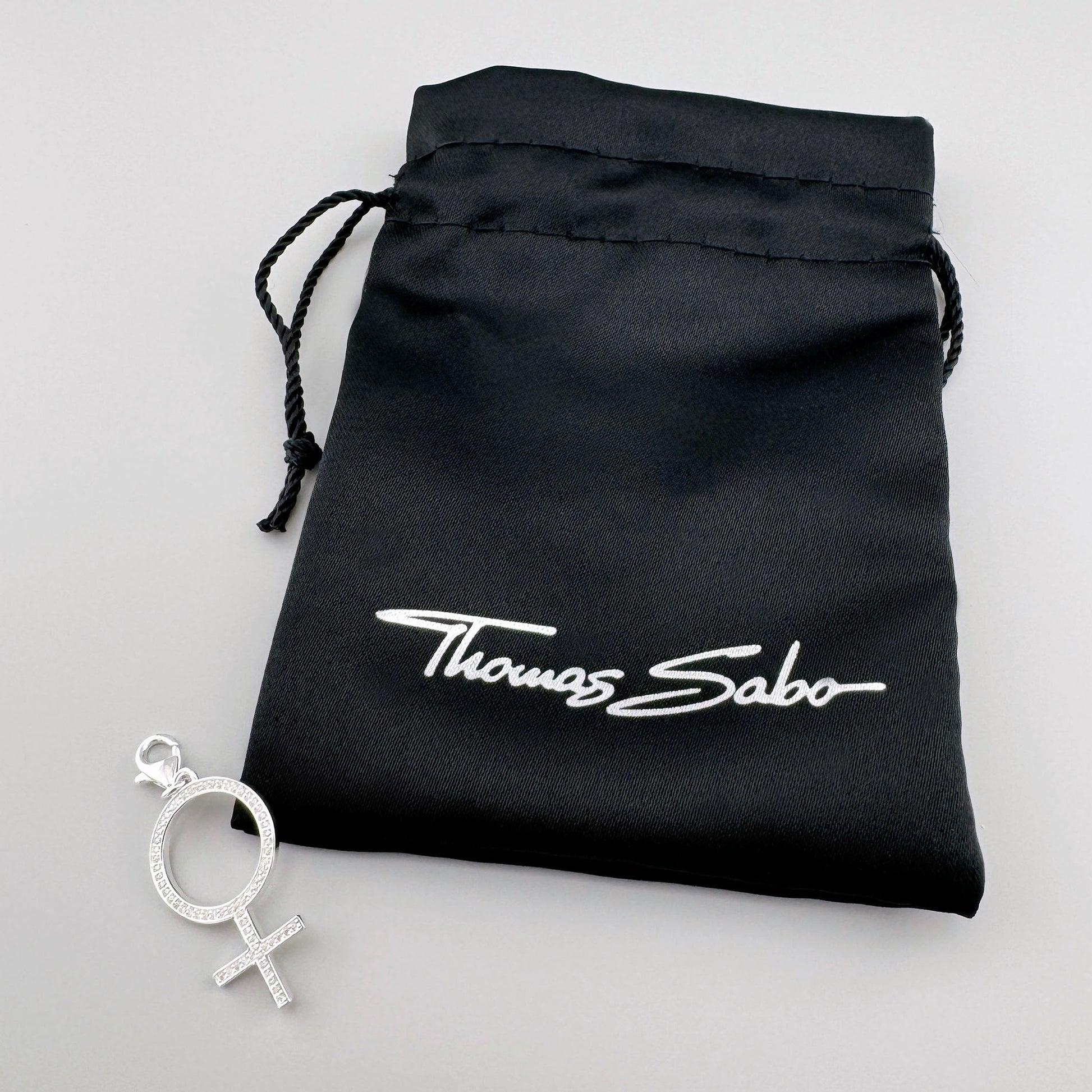 Srebrna zawieszka symbol kobiety Thomas Sabo obok czarnego firmowego woreczka