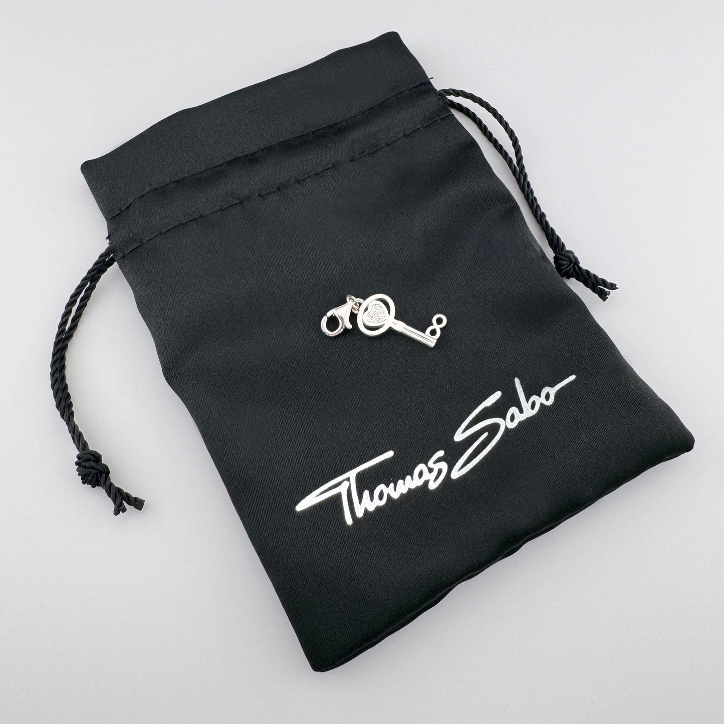 Silver Thomas Sabo key charm displayed on its branded black pouch