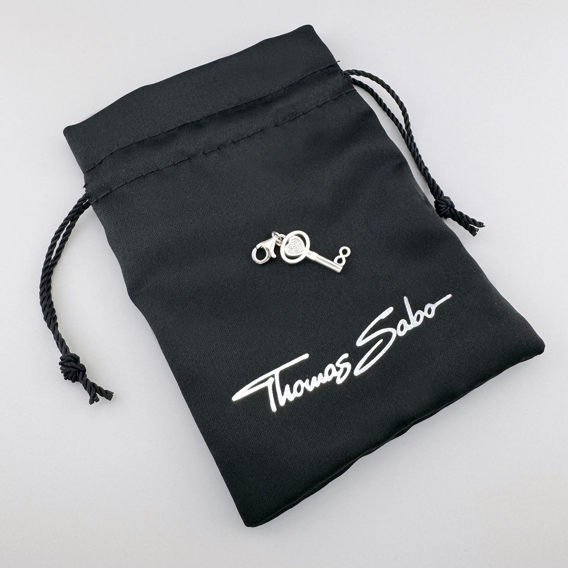 Silver Thomas Sabo key charm displayed on its branded black pouch
