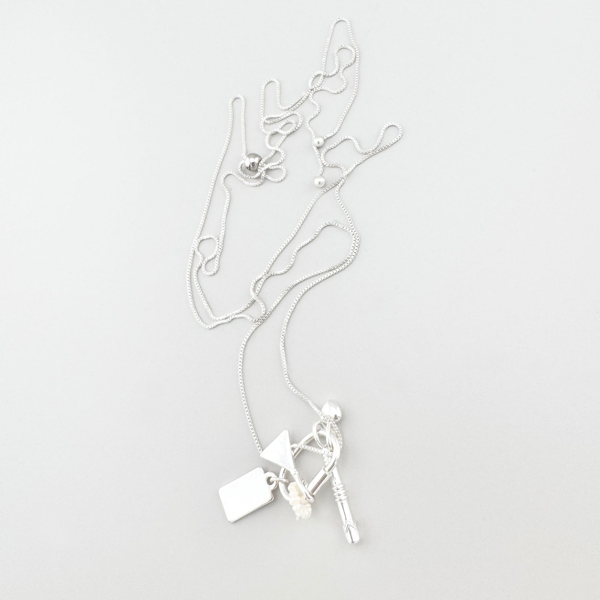 Collier argenté Pilgrim avec breloques disposé sur fond clair