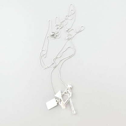 Collier argenté Pilgrim avec breloques disposé sur fond clair