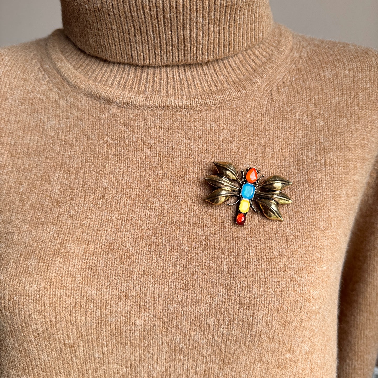 Gold-toned insect brooch worn on beige knitwear