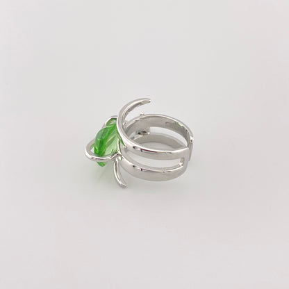 Green crystal ring with silver band placed on a tree branch for contrast