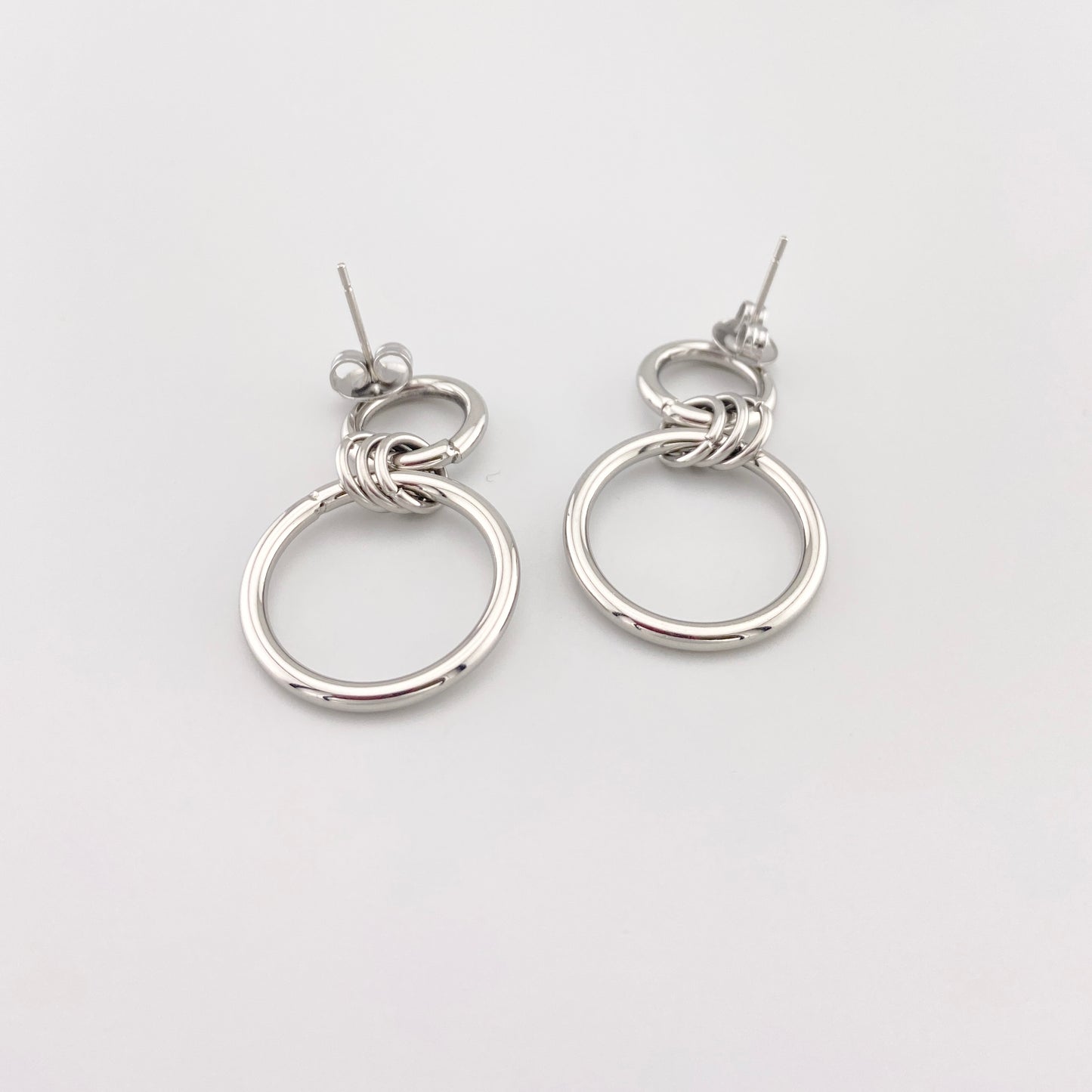 Сережки-кільця IRL на світлому мармурі, подвійні кола з полірованої сталі, чистий мінімалізм