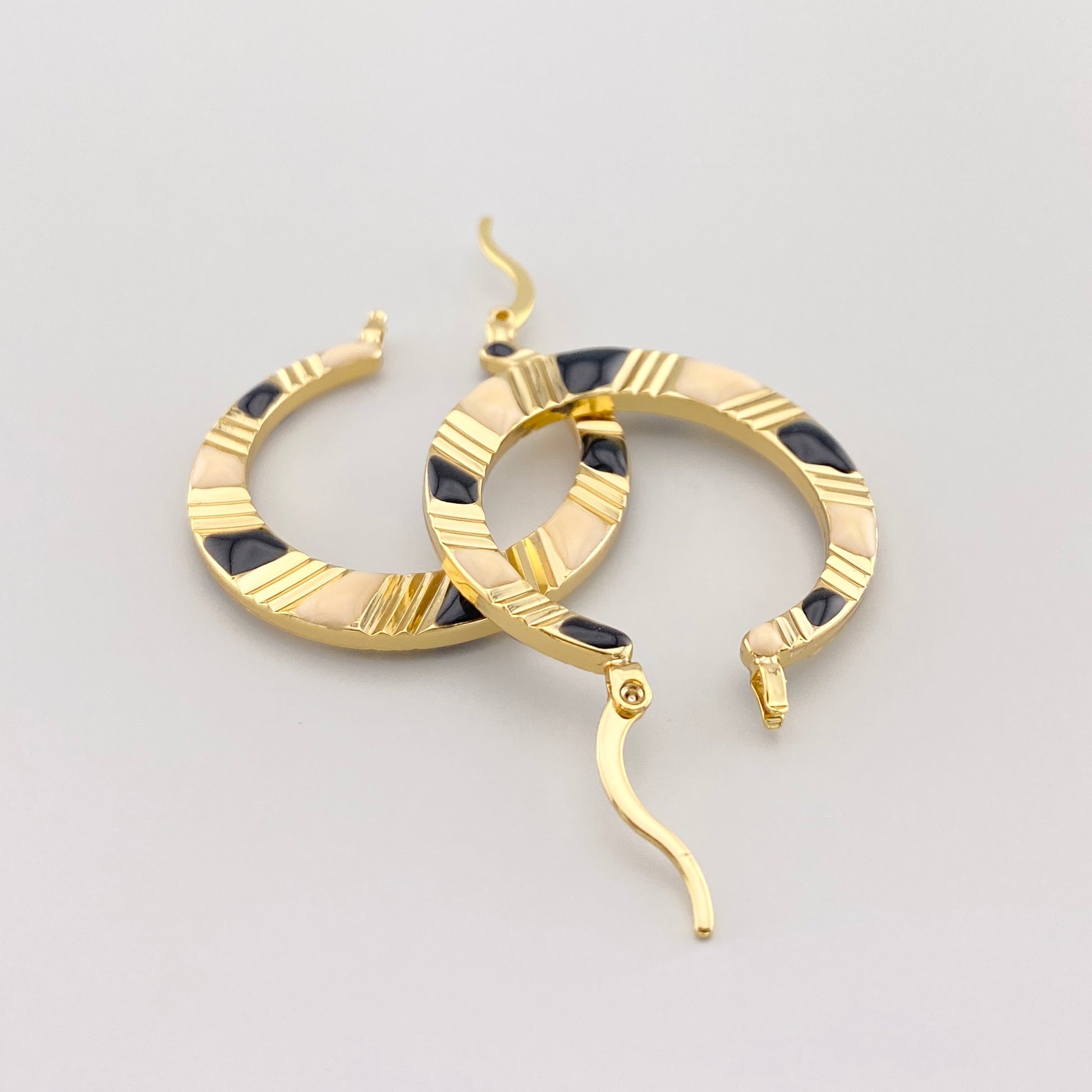 Pendientes dorados con esmalte negro y crema, vista lateral que destaca la precisión y detalles grabados