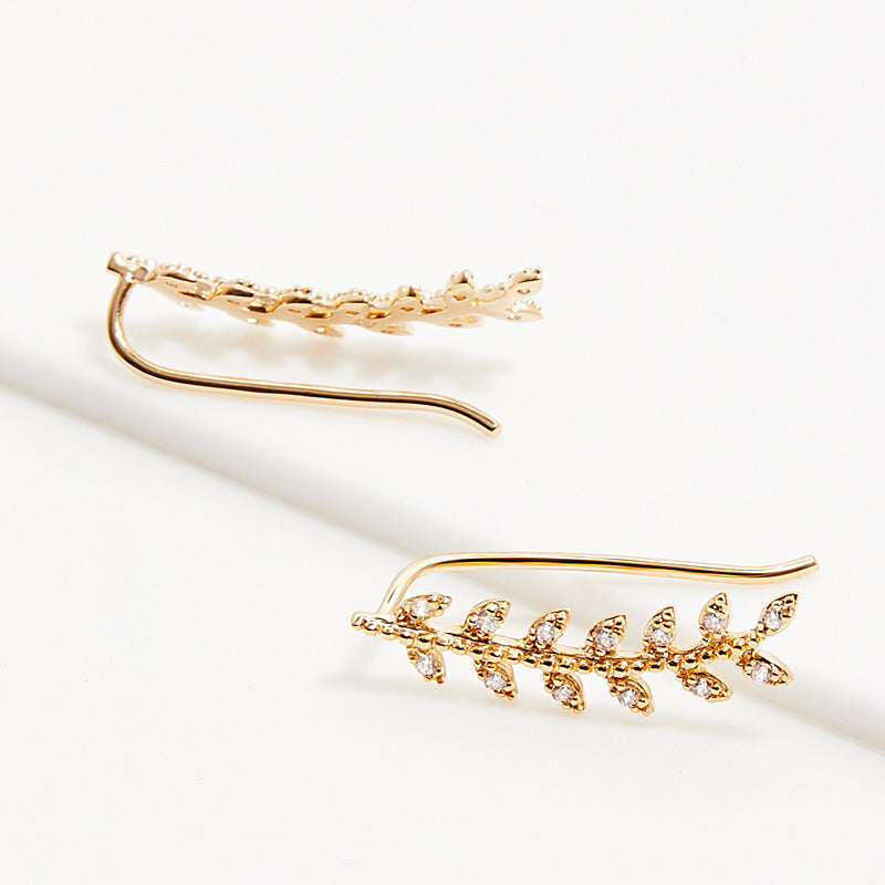Nausznice IRL doradas con circonitas, línea fina de hojas sobre fondo neutro