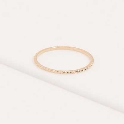 Anillo minimalista IRL chapado en oro con detalle trenzado sobre superficie clara